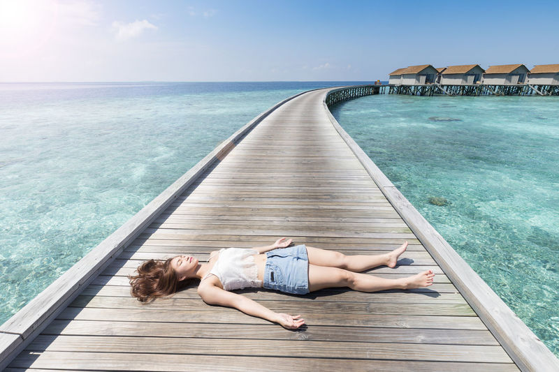 Woman lying on boardwalk amidst sea against sky