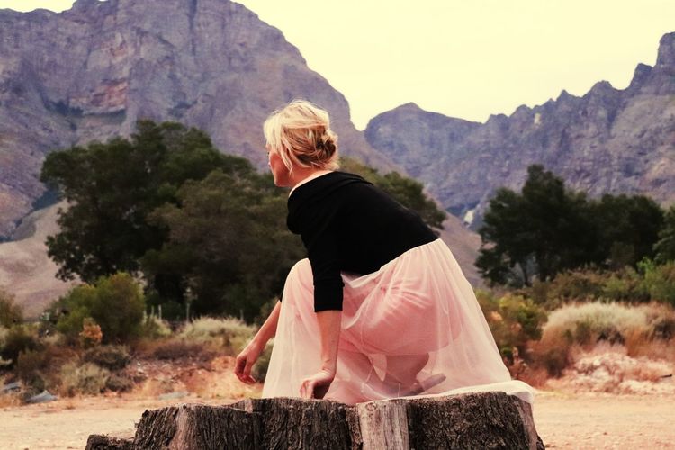 Side view of woman crouching on tree stump against mountains