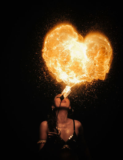 Woman blowing heart shape firework at night