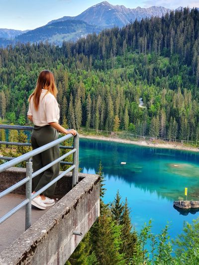 Woman sitting on railing by lake against mountain