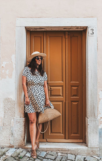 Full length portrait of a young woman in polka dot dress in front of old door.