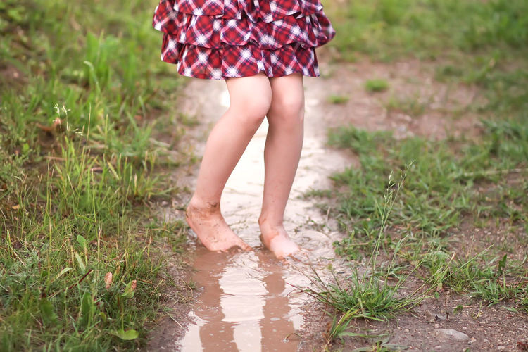 Barefoot girl walks through a puddles of water after the summer rain in countryside.