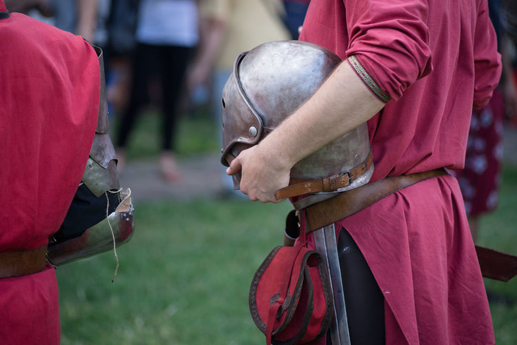 Midsection of medieval knight holding helmet while standing on field