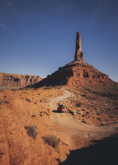 An orange car is driving through the valley of gods, utah