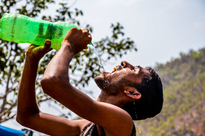 Man drinking water from bottle against sky