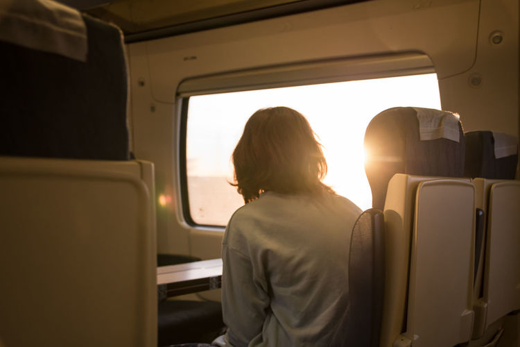 The traveling young girl looks dreamily from the window of the train into the sunrise