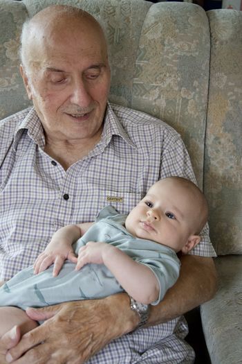 Portrait of cute baby boy sitting on grandfather hands at home