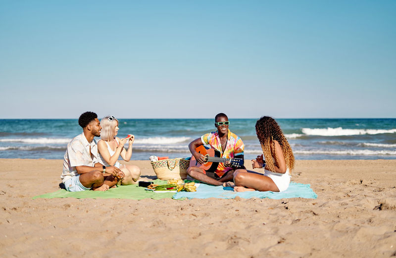 Side view of woman sitting at beach against clear sky