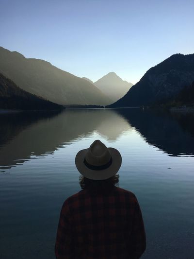 Rear view of man wearing hat while looking at lake against sky