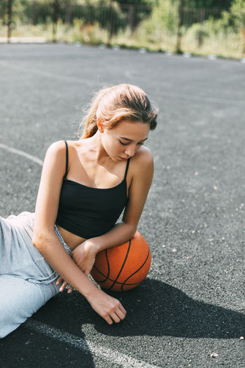 A basketball player is sitting on a sports field with a basketball and looks away. sports, fitness