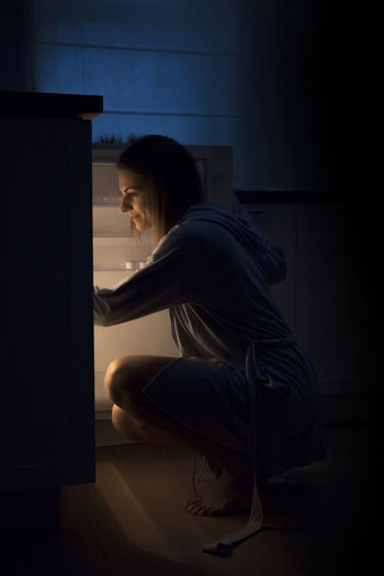 Side view of woman searching in refrigerator at darkroom