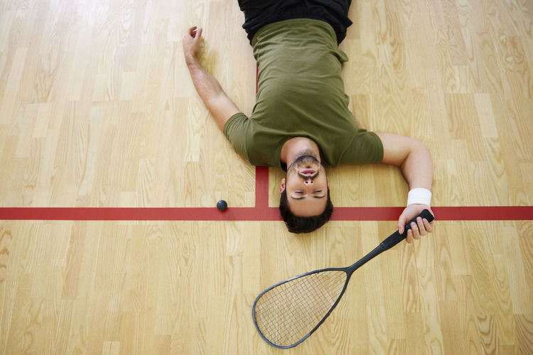 High angle view of tired man lying on hardwood floor at court