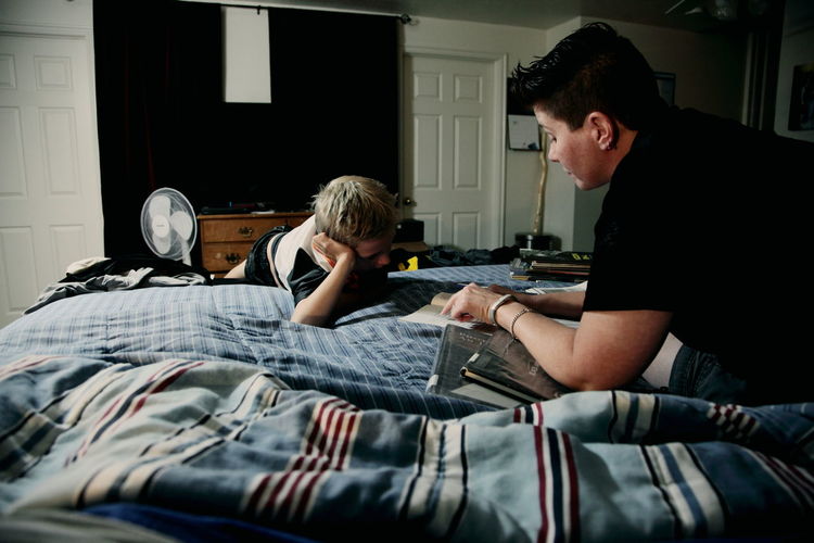 Mother assisting son in homework on bed
