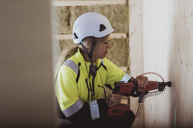 Female builder using work tool on wall while working at construction site
