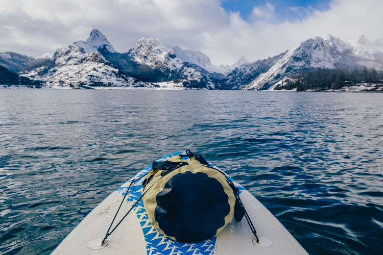 Picturesque view of stone hills in snow on shore and bag placed on nose of shallop floating on water surface