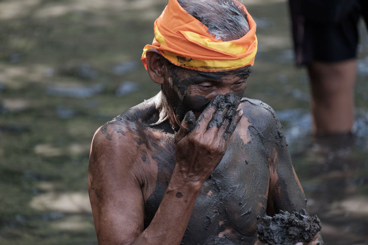 Close-up of shirtless man applying mud on body