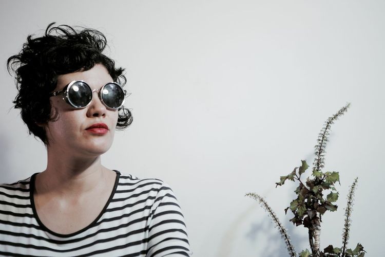 Woman wearing sunglasses against wall