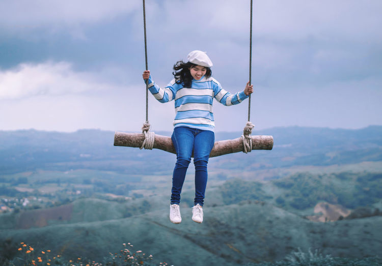 Smiling young woman swinging over landscape