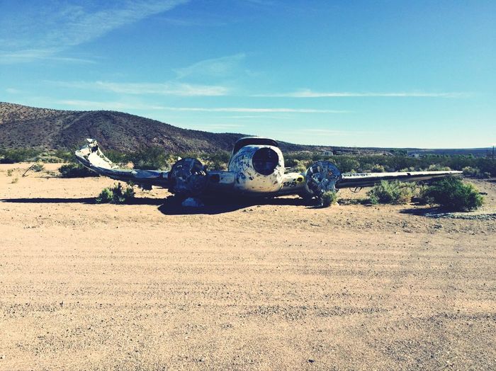 Abandoned crashed airplane on field by dirt road against sky