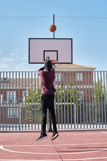 Rear view of man standing by basketball hoop against sky