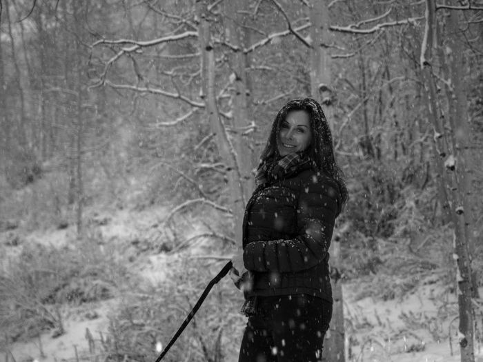 Portrait of smiling woman standing in forest during snowfall