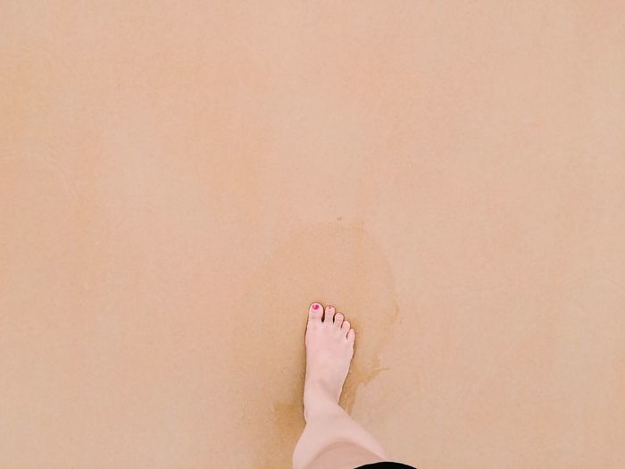Directly above view of woman feet on wet sand