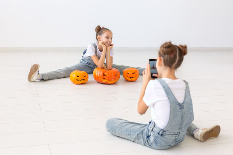 Mother and girl sitting on floor against orange wall