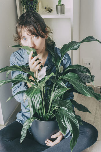 Portrait of young woman holding plant at home