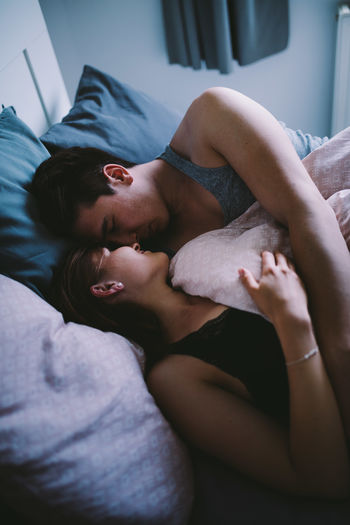 High angle view of young couple romancing while lying on bed at home