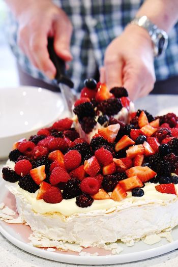 Midsection of man cutting pavlova on table