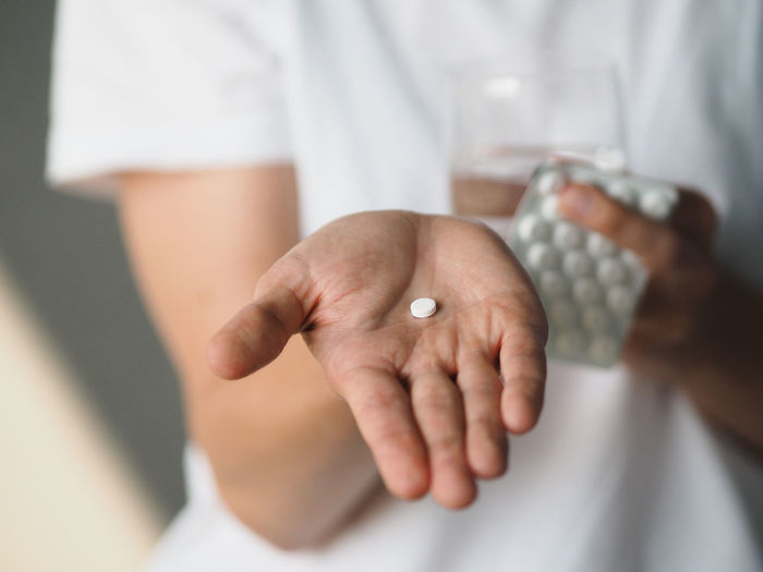 Woman holds in hand a white pill and a glass of water.