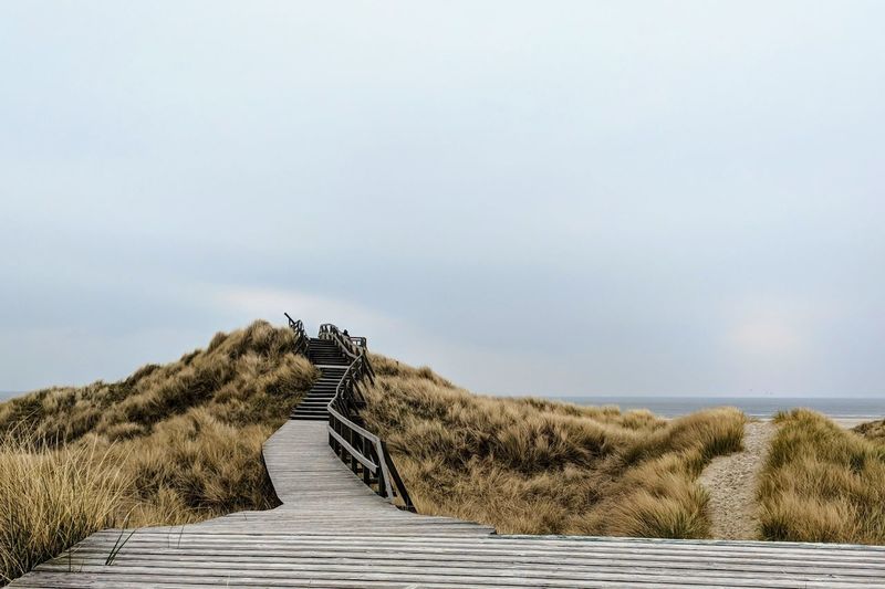 Empty boardwalk at beach against sky