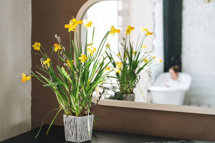 Yellow flowers near mirror in bathroom with enjoing young woman, treat yourself