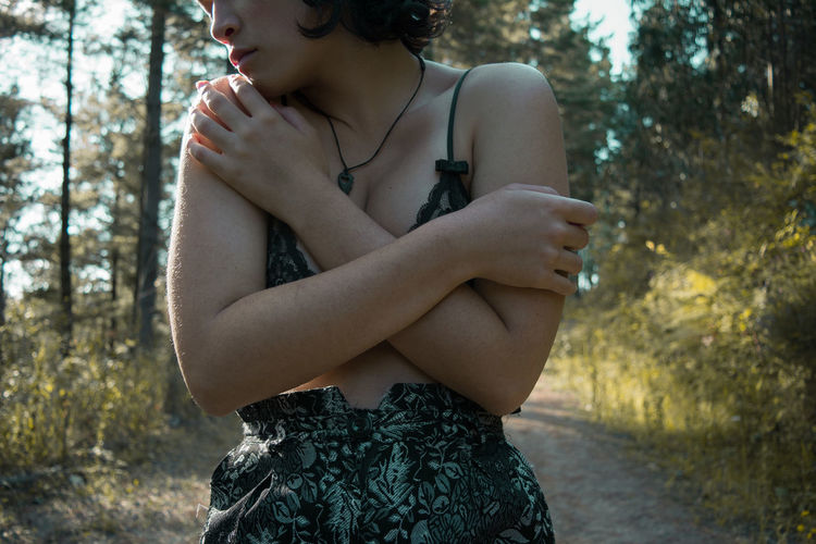 Midsection of woman hugging self while standing in forest