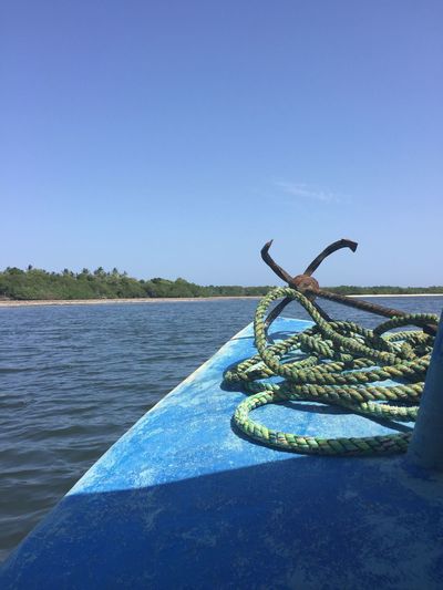 Rusty anchor and rope on boat in lake against sky