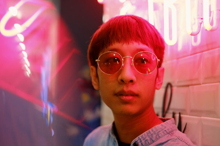 Close-up of man in sunglasses by illuminated store 