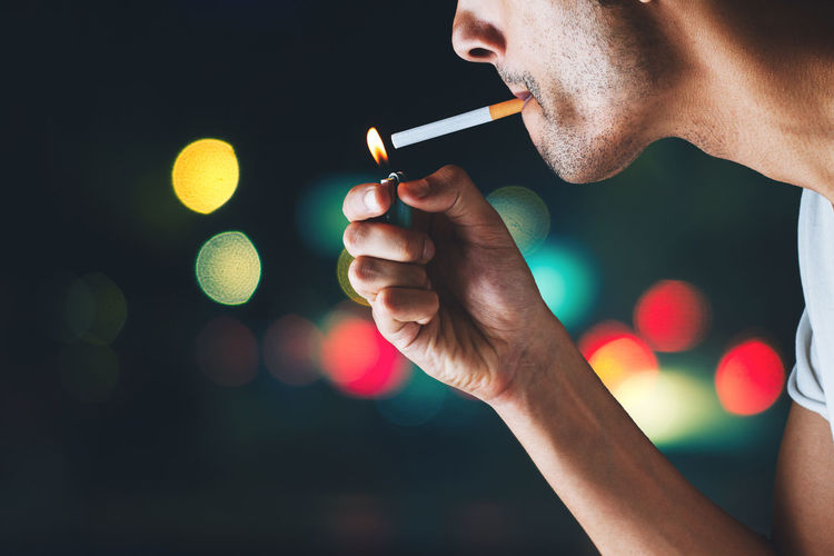Midsection of man smoking cigarette at night