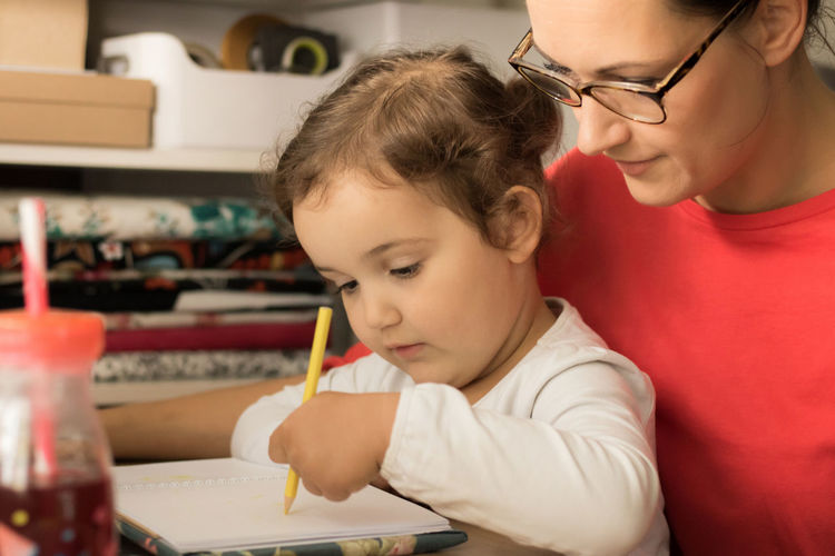 Mother assisting daughter in writing homework at home