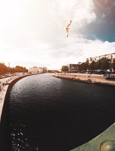 Man jumping over river in city against sky