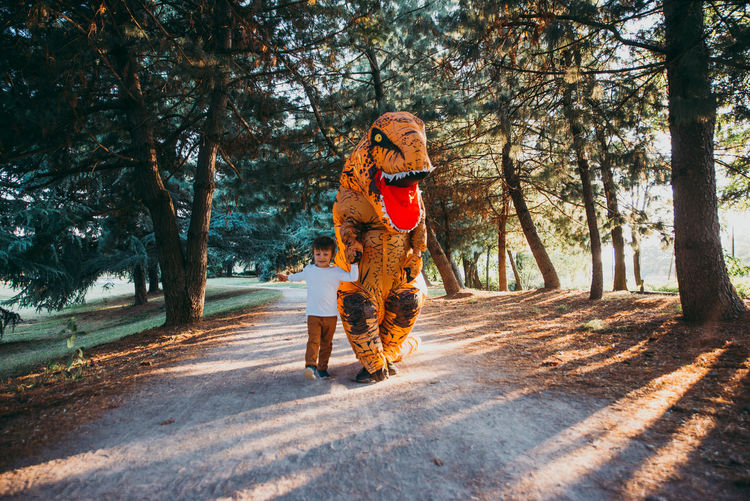 Boy walking with person wearing dinosaur costume in park