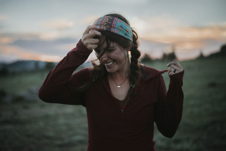 Happy woman removing headband while standing at field during sunset