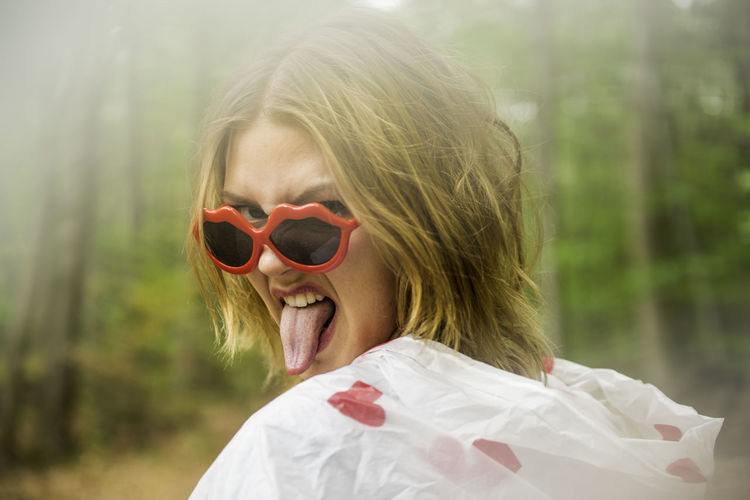 Portrait of young woman wearing sunglasses while sticking out tongue outdoors