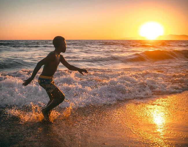 Boy running on beach against sky during sunset