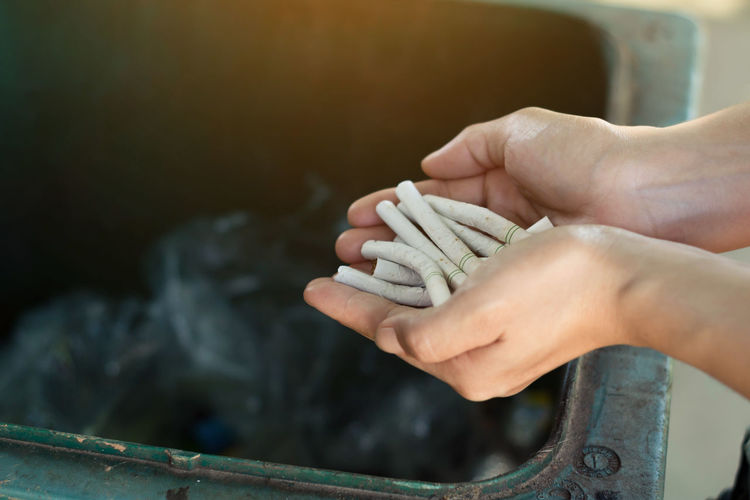 Close-up of hand holding cigarettes over garbage bin