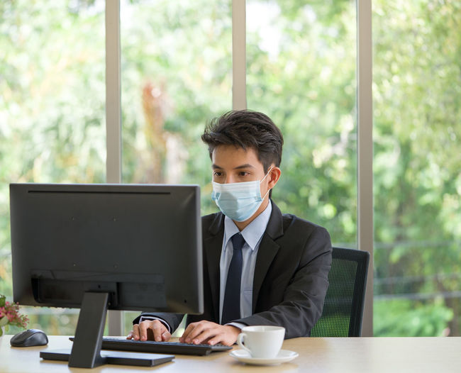 Young businessman wearing flu mask using computer at office