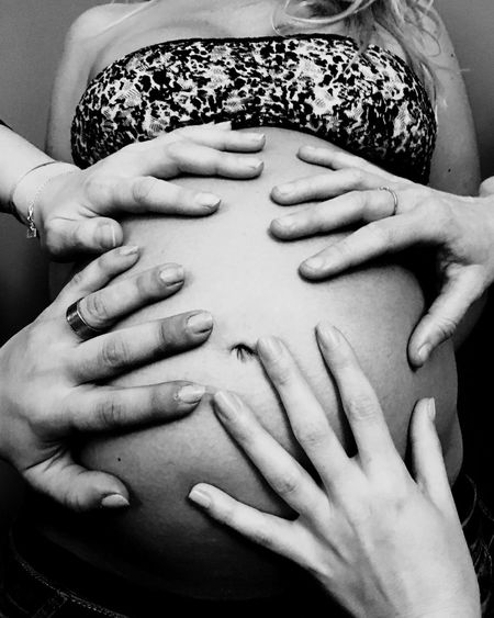 Cropped friends putting hands on pregnant woman belly at home