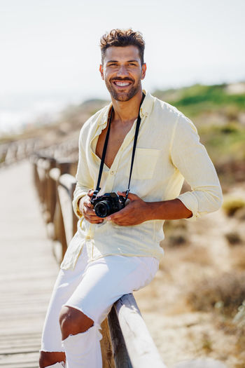 Portrait of smiling man holding camera sitting on railing
