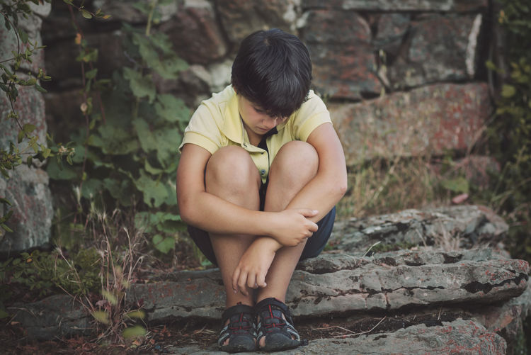Sad boy sitting against stone wall
