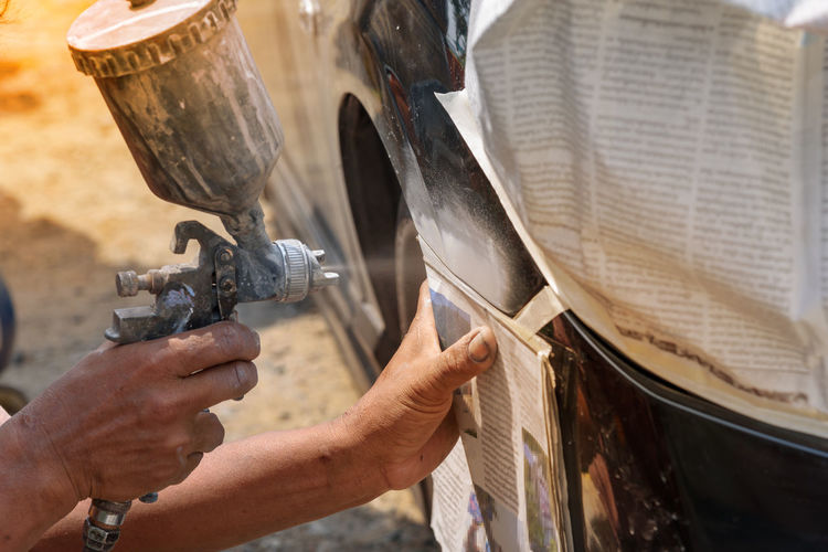 Cropped image of worker spraying paint on car
