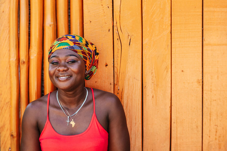 African woman with a hopeful happy smile standing against a painted wooden wall